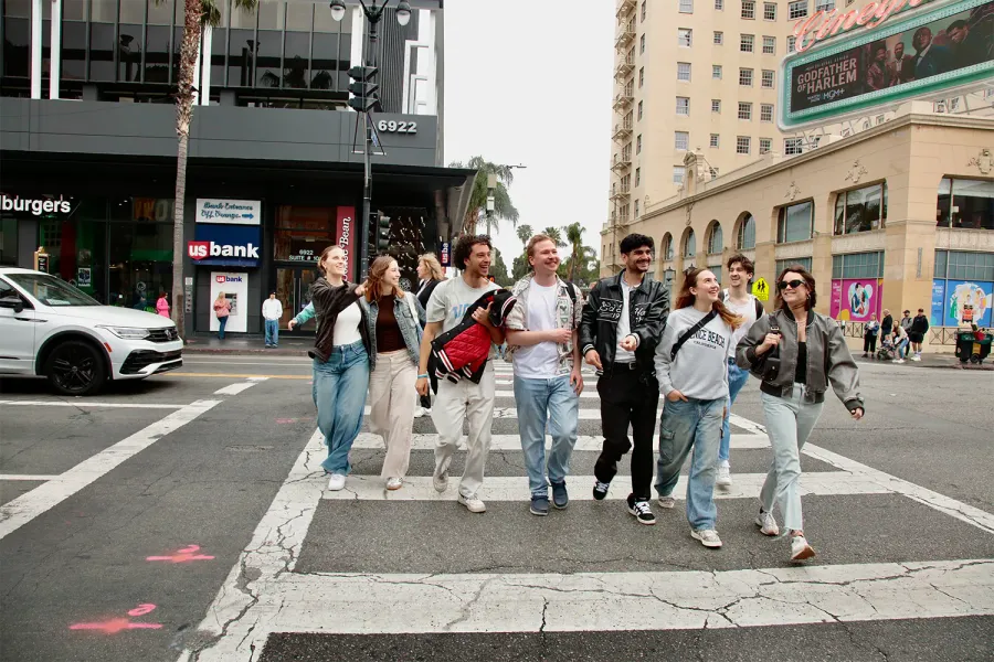 Teilnehmende sitzen in einer Reihe auf dem Bordstein vor einem großen Wandgemälde in Los Angeles
